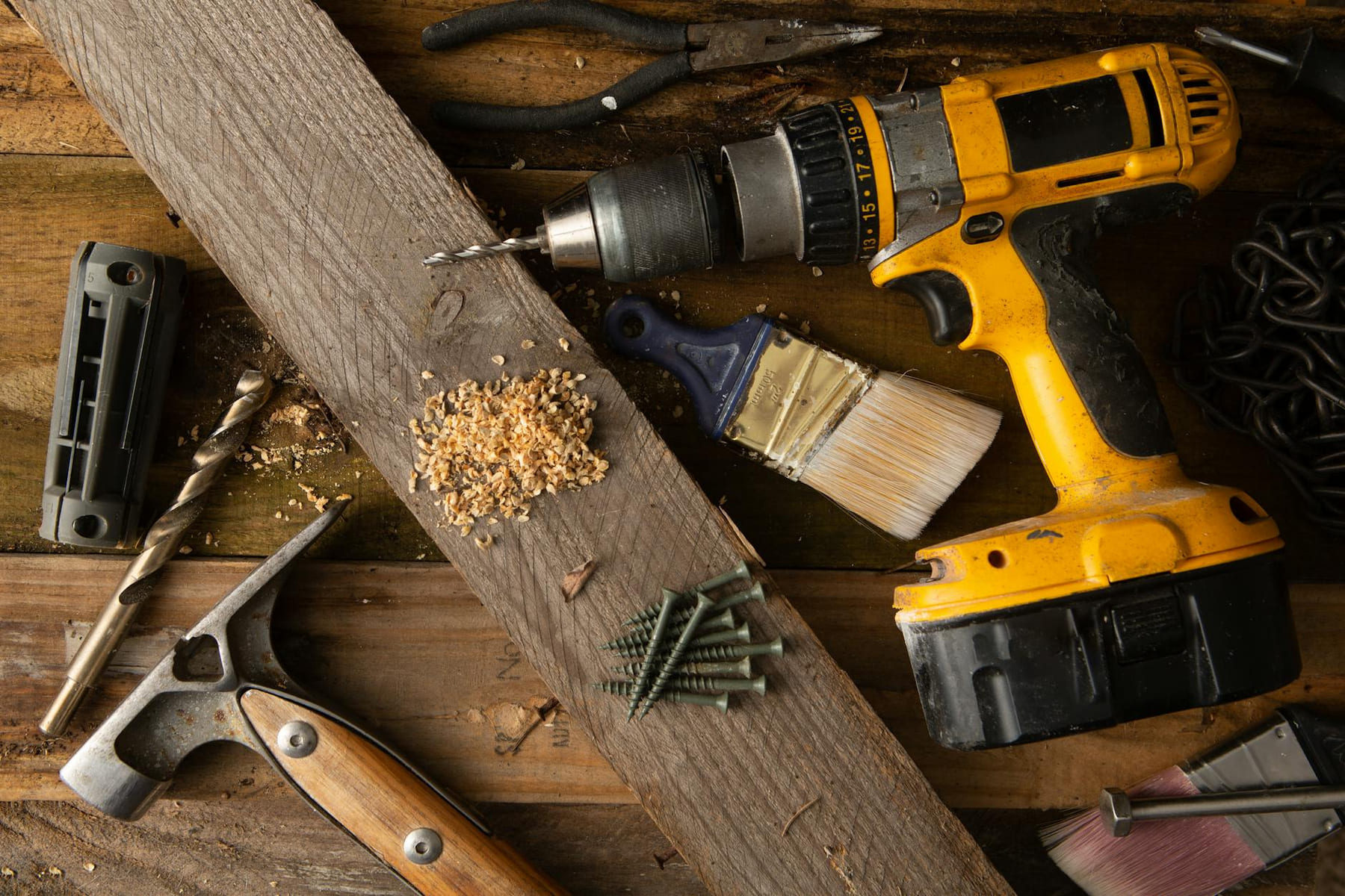 A close-up of various tools including a drill, hammer, and paintbrush on a wooden workbench. on Hammer & Home