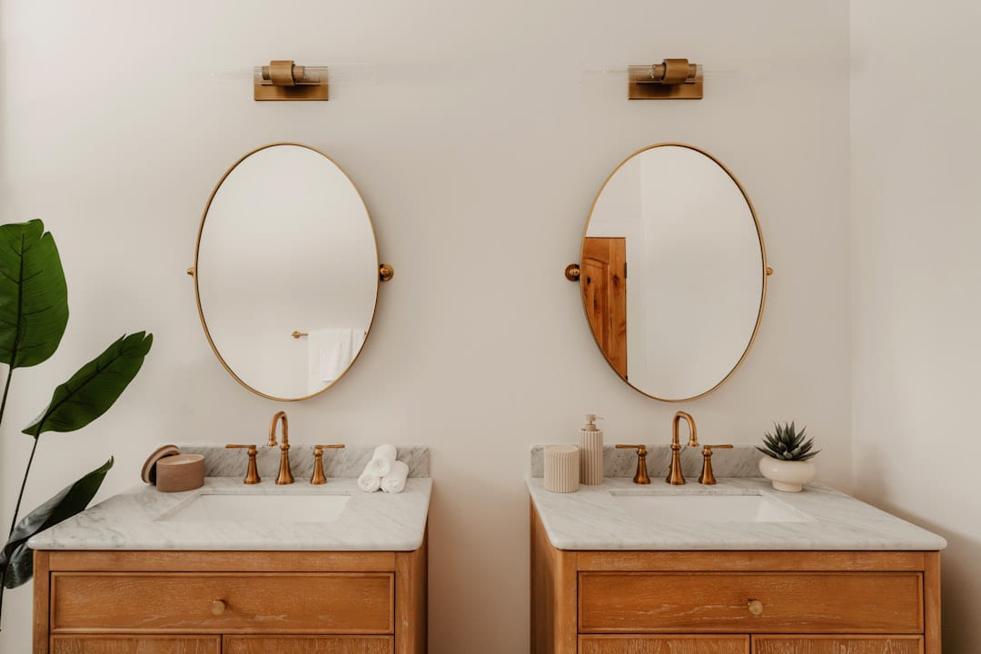 Two wooden vanities with oval mirrors and gold fixtures. on Hammer & Home