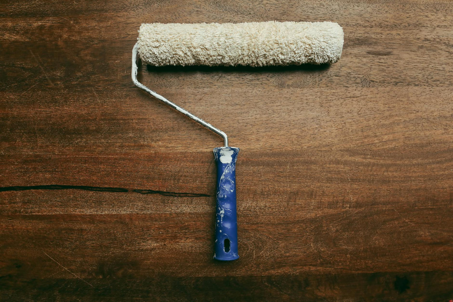 A worn paint roller placed on a wooden surface, ideal for DIY home improvement visuals. on Hammer & Home