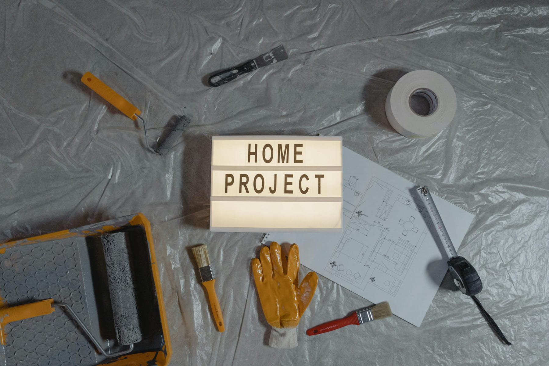 Flat lay of home improvement setup with tools, gloves, and floor plan for DIY projects. on Hammer & Home