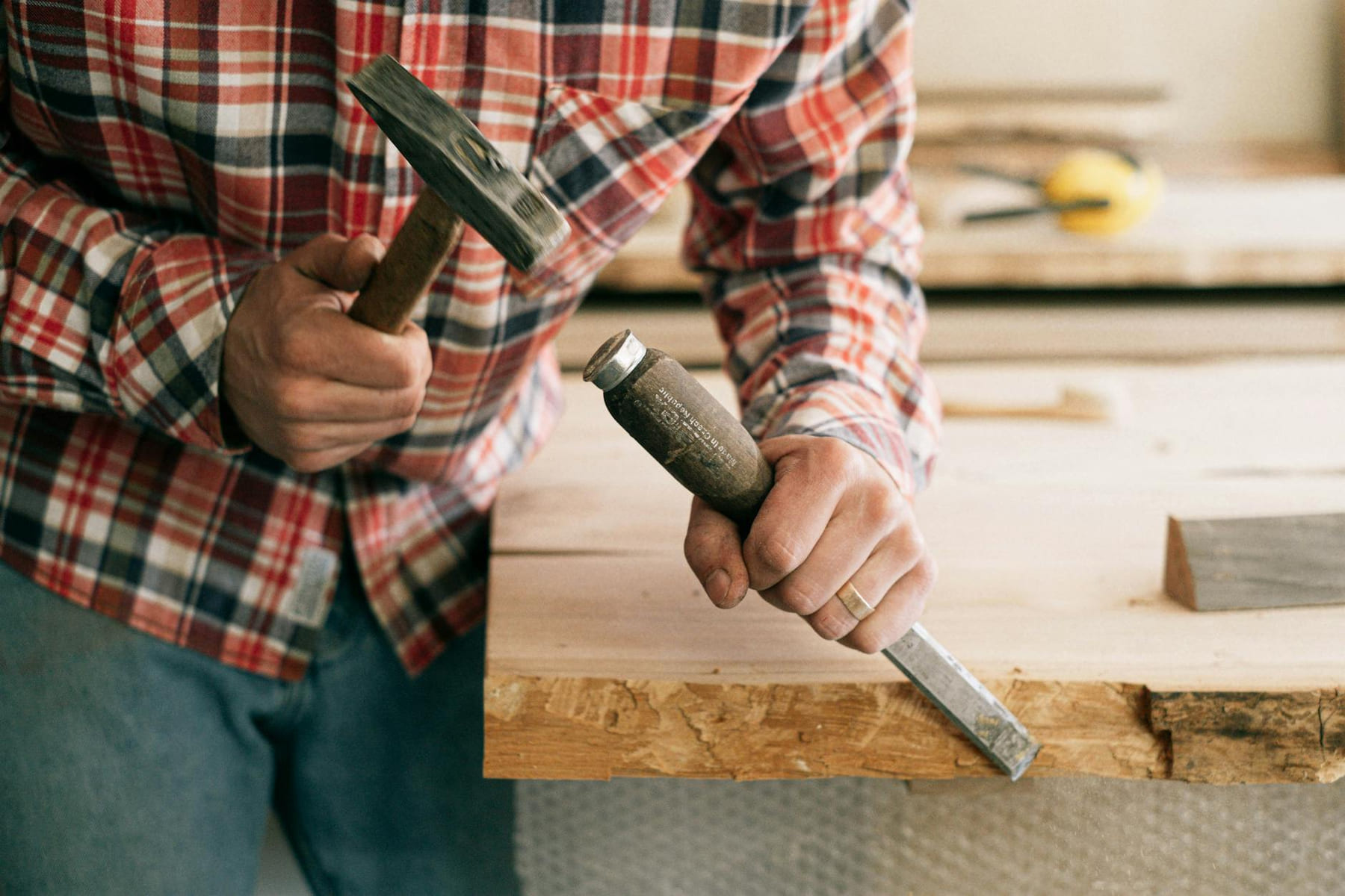 Detailed view of a carpenter using a hammer and chisel on a wooden plank, showcasing craftsmanship. on Hammer & Home