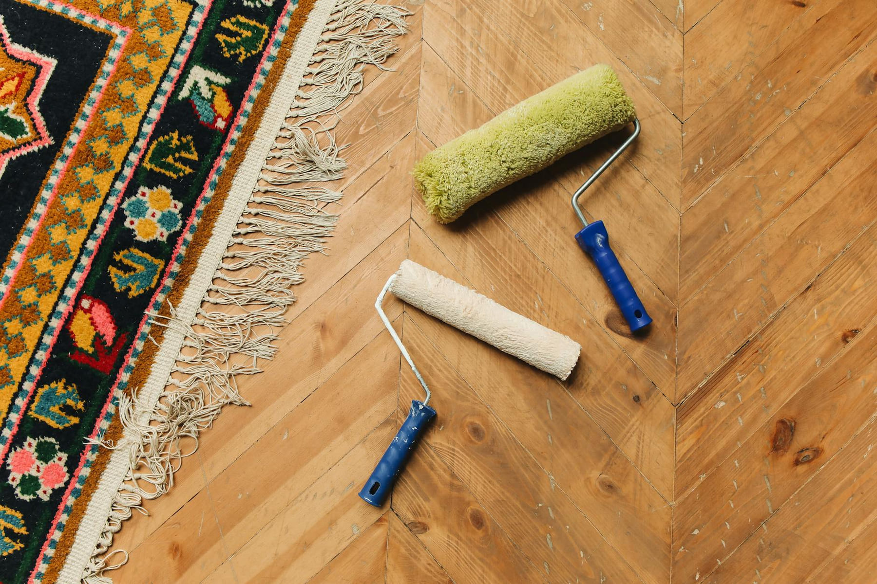 Two paint rollers on a wooden floor next to a colorful rug, symbolizing home renovation. on Hammer & Home